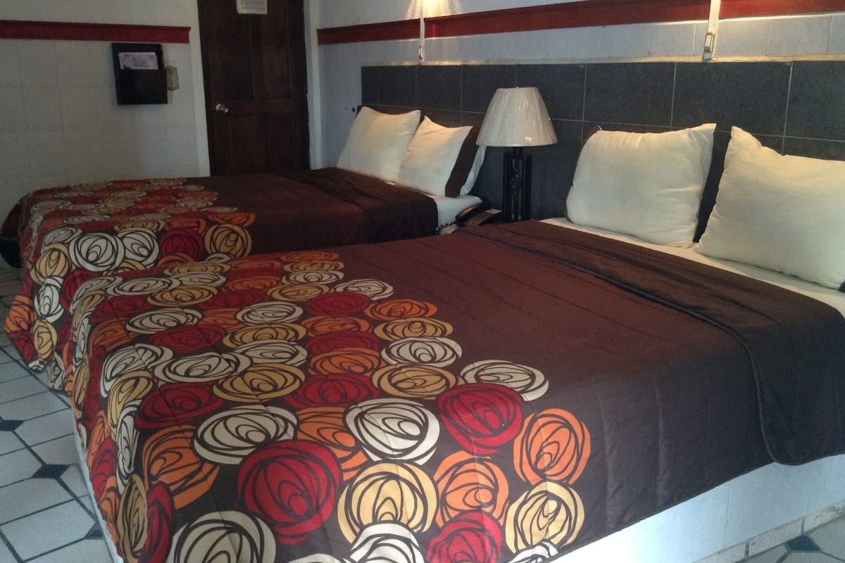 A hotel room with two beds, each with a headboard and a bedside lamp.
