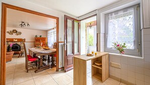 A modern kitchen with a wooden island, a dining area with a fireplace, and a view through a window with a floral curtain. - Tildren - Guern - Gîte (GUERN)