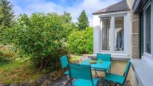 A patio with a table and chairs, a window with a view of greenery, and a stone pathway. - Tildren - Guern - Gîte (GUERN)