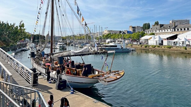 A marina with boats docked, a wooden boat with passengers, and a cityscape in the background. - Tildren - Guern - Gîte (GUERN)