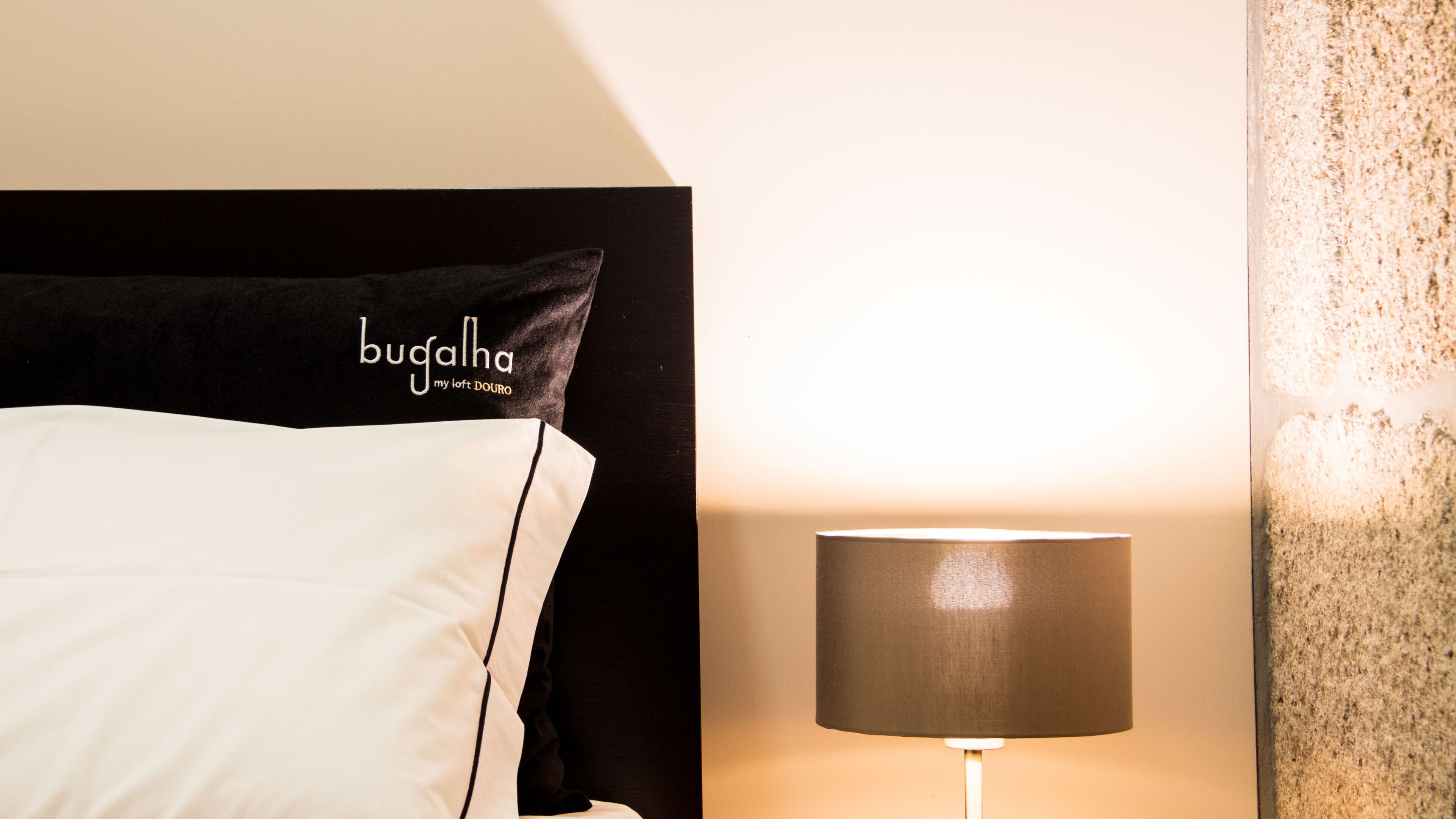 A bed with a black headboard and a pillow labeled "bugalha my loft DOURO".