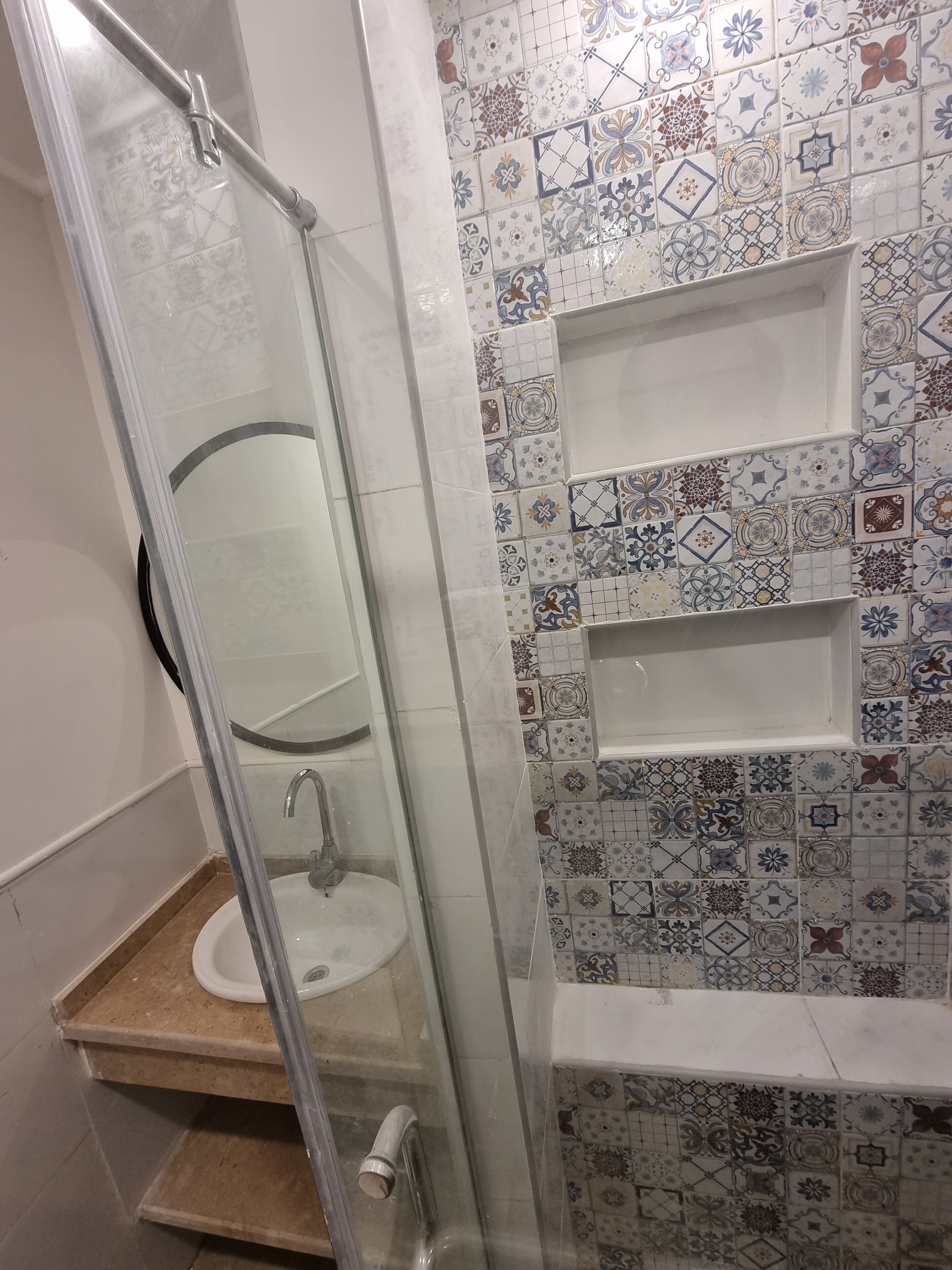 A bathroom with a glass shower enclosure, a sink, and a tiled wall with decorative patterns.