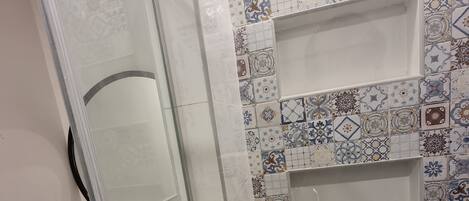 A bathroom with a glass shower enclosure, a sink, and a tiled wall with decorative patterns.