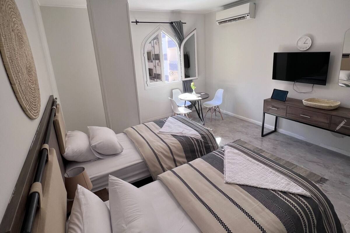 A hotel room with two beds, a desk, a TV, and a window.