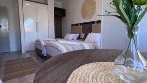 Quarto de hotel moderno com cama, mesa redonda trançada e um vaso com flores.
