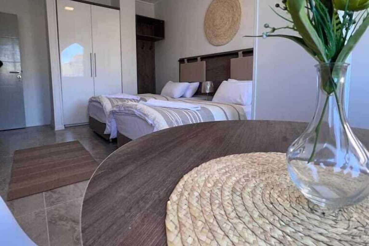 A modern hotel room with a bed, a round woven table, and a vase with flowers.
