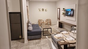 Um espaço compacto para viver, com cozinha compacta, sofá, mesa de jantar posta para quatro pessoas e televisão de tela plana na parede.