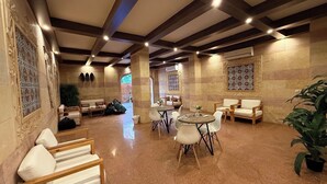 Um hall amplo com teto alto, paredes de pedra e diversos espaços de estar, incluindo sofás e mesas.