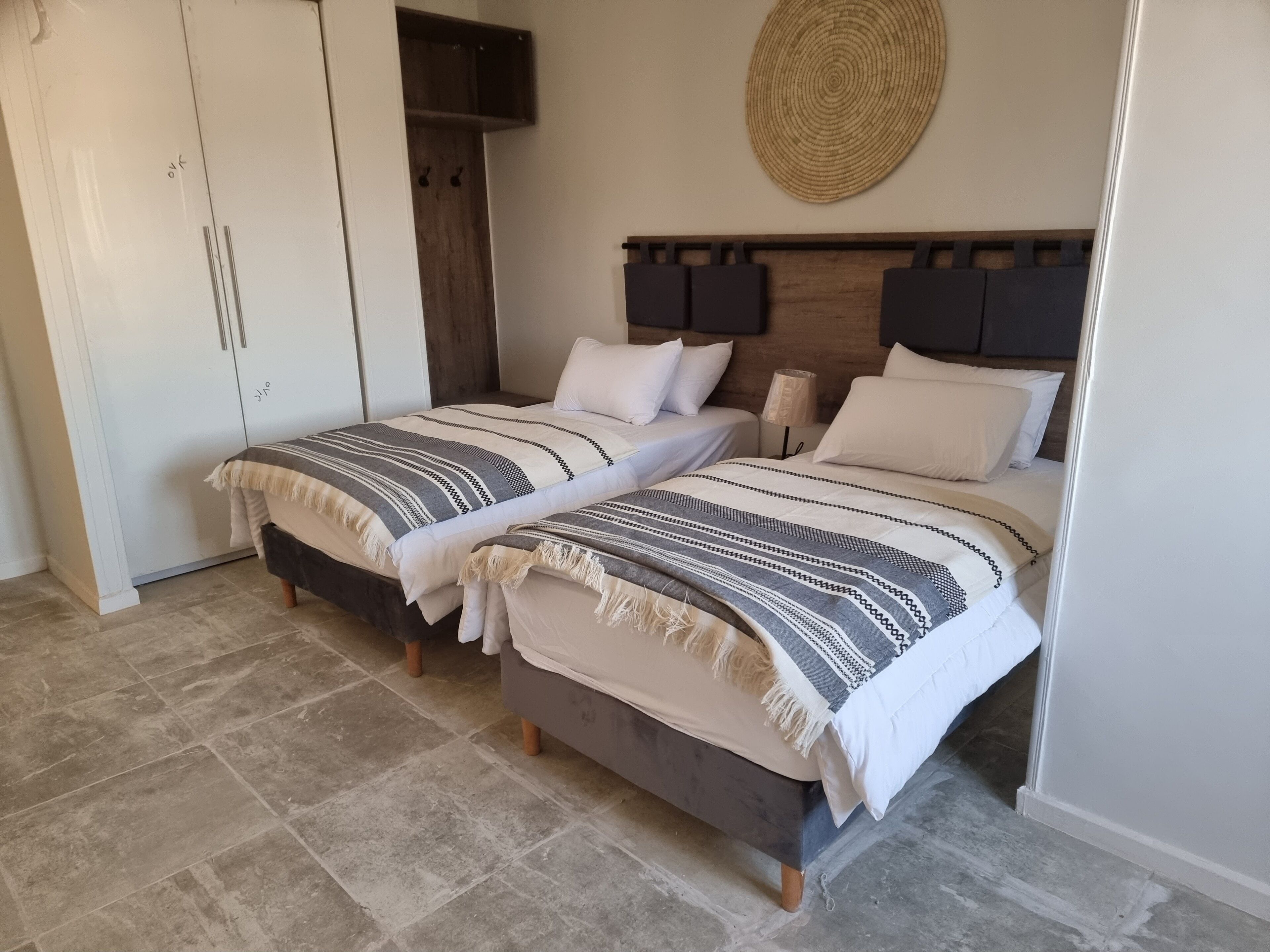A bedroom with two beds, a wardrobe, and a woven wall decoration.