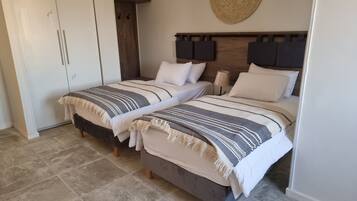 A bedroom with two beds, a wardrobe, and a woven wall decoration.