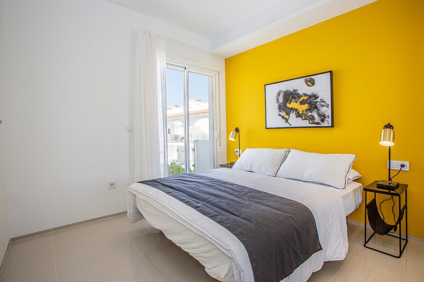A bedroom with a bed, a window with curtains, a yellow wall, and a painting.