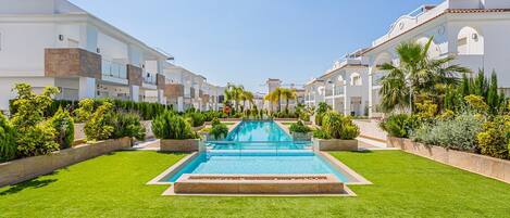 A resort with a central swimming pool, surrounded by well-maintained lawns and tropical plants.