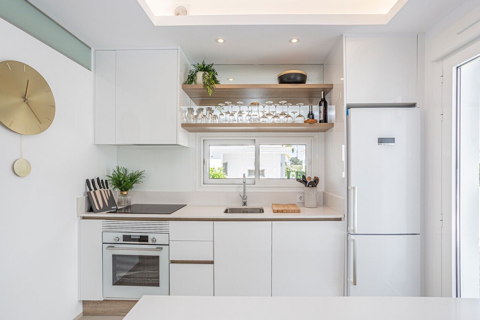 Een moderne keuken met witte kasten, een ingebouwde oven, een spoelbak en een raam boven het aanrecht.