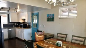 Uma cozinha moderna com armários brancos, uma porta azul e um espaço de jantar com mesa e cadeiras de madeira.