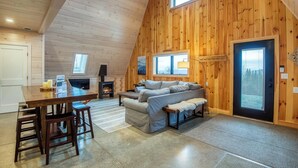 Een knus chaletinterieur met houten details, een bank, een eettafel met stoelen en een open haard.