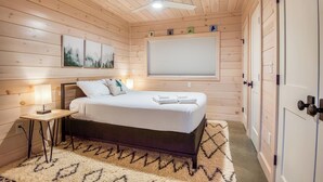 Een gezellige slaapkamer met een bed, nachtkastje, lamp, plafondventilator en een raam met zonwering.