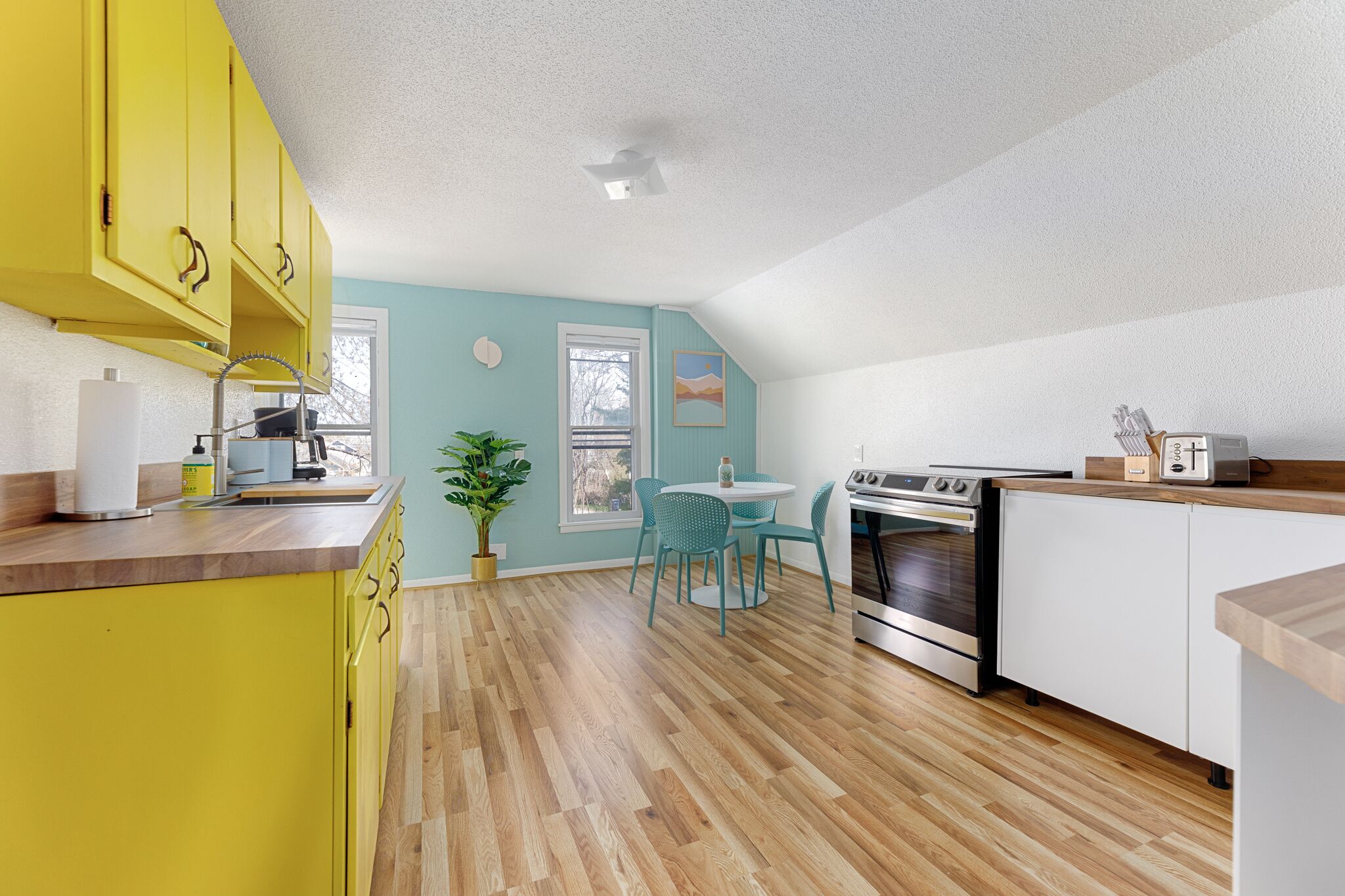 Une cuisine avec des meubles de couleur jaune, un plan de travail en bois, une cuisinière et un coin repas avec des chaises.