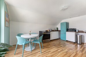 Une cuisine compacte avec une table blanche et des chaises turquoise, un four à micro-ondes et un petit réfrigérateur.