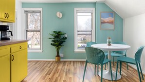A kitchen with yellow cabinets, a round table with teal chairs, and a potted plant. - 70's Vibe | Beach | Downtown | AC | Nightlife | (Traverse City)