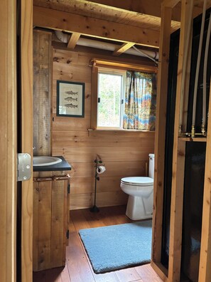 A wooden cabin bathroom with a sink, toilet, and window. - Cozy, Off-Grid Camp on Spectacle Pond w/ private water frontage! (Osborn)