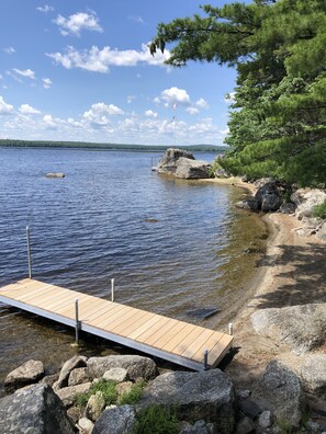 Une jetée en bois s’étendant sur un lac paisible, entourée de rochers et d’arbres.