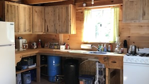 A rustic kitchen with wooden cabinets, a white refrigerator, a stove, and a sink. - Cozy, Off-Grid Camp on Spectacle Pond w/ private water frontage! (Osborn)