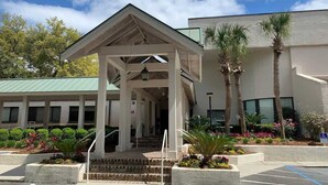 A building with a covered entrance, steps leading up to it, and a parking lot with marked spaces. - Ocean Villa C147 - Steps from Beach and Pool (Hilton Head Island)