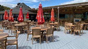 An outdoor patio with wooden tables and chairs, red umbrellas, and a wooden roof structure. - Ocean Villa C147 - Steps from Beach and Pool (Hilton Head Island)