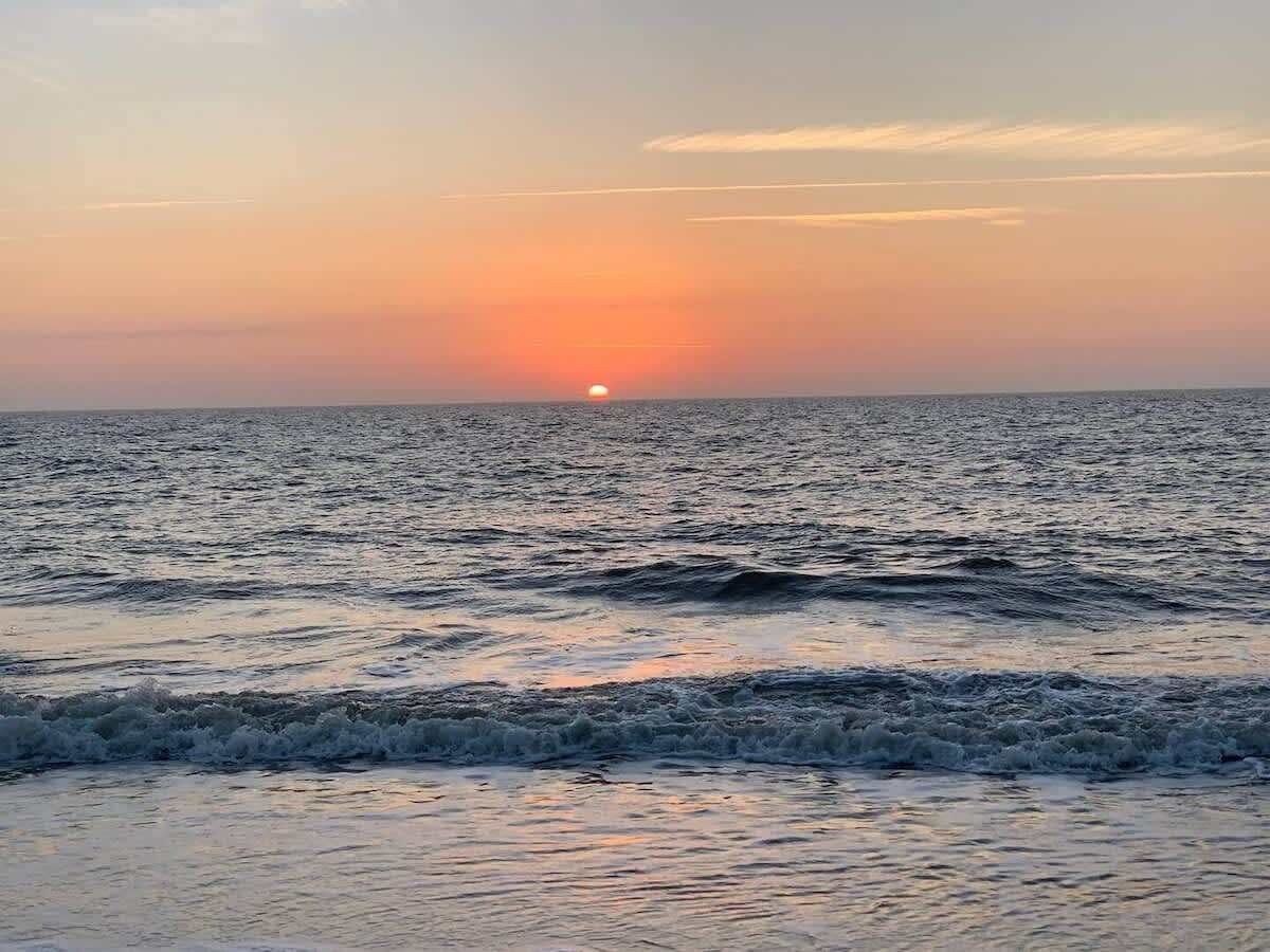 A sunset over the ocean with waves approaching the shore.