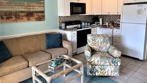 A compact living space with a kitchenette, a sofa, a floral armchair, and a coffee table. - Ocean Villa C147 - Steps from Beach and Pool (Hilton Head Island)