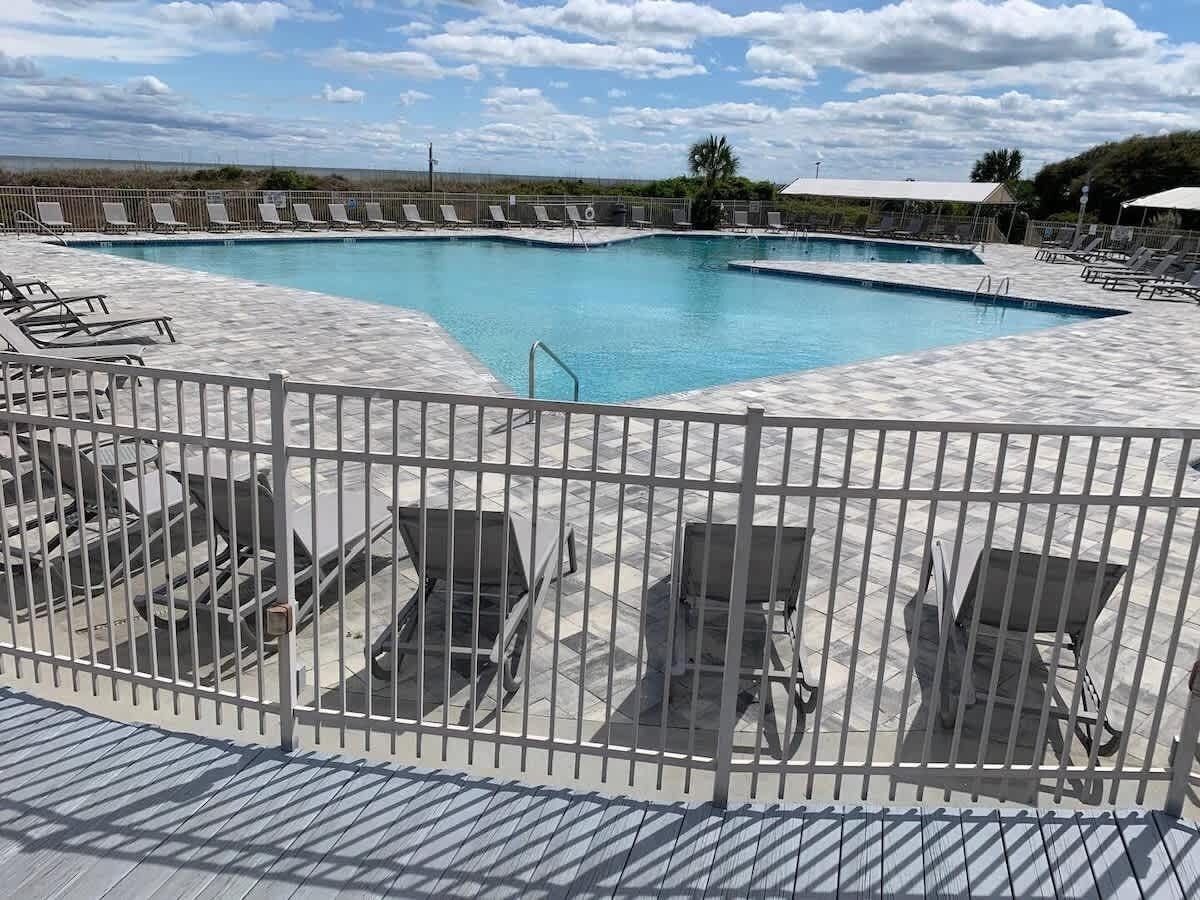 A pool area with multiple lounge chairs and a fenced deck.