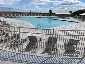 Un espace piscine doté de nombreuses chaises longues et d’une terrasse délimitée par une clôture.