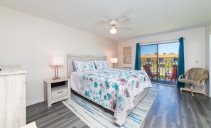 A bedroom with a bed, bedside tables, a lamp, a chair, and a balcony with a view. - Seabreeze Escape at Ponce Landing 34 (St. Augustine)