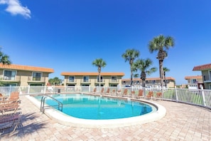 A swimming pool surrounded by lounge chairs and palm trees, with buildings in the background. - Seabreeze Escape at Ponce Landing 34 (St. Augustine)