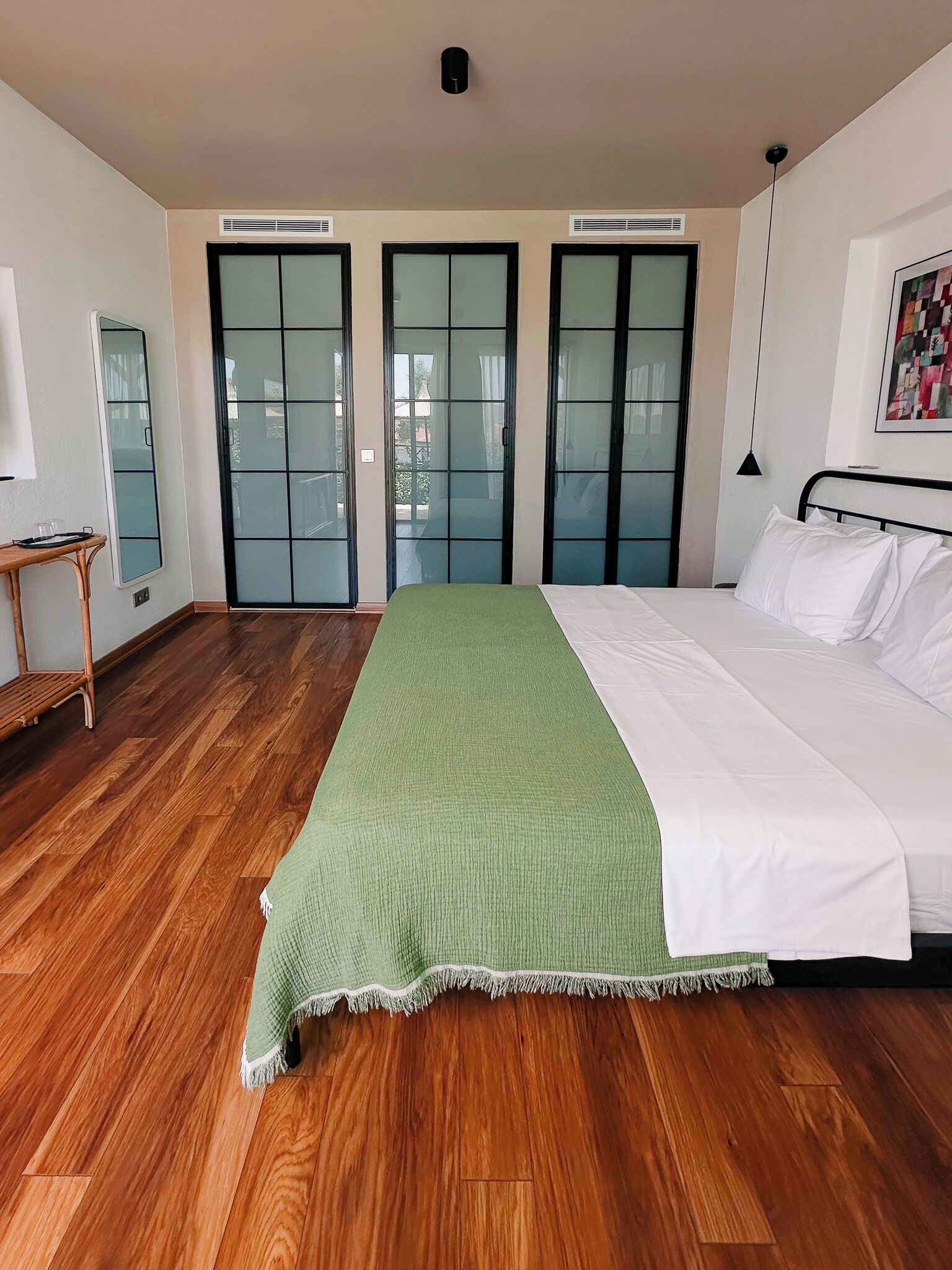 A bedroom with a large bed, wooden flooring, and sliding glass doors leading to an outdoor area.