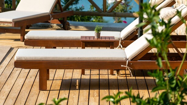 A wooden deck with lounge chairs and a thatched umbrella, overlooking a body of water with boats. - Boho Garden Selimiye (Marmaris)