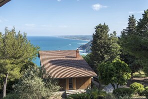 Una casa sul lungomare con tetto in tegole, immersa nel verde e con vista mare.