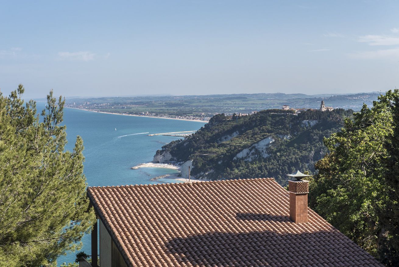 A coastal view with a tiled roof, a lighthouse, and a beach in the background.