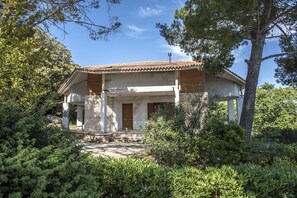 Uma casa de dois andares com telhado de telhas, varanda da frente e jardim com diversas plantas.