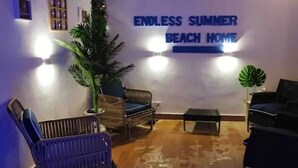 Una habitación con un cartel que dice 'Endless Summer Beach Home', muebles de mimbre, una planta en maceta y una pequeña mesa.
