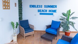 Una habitación con muebles de mimbre, una planta en maceta y una pared con el texto 'ENDLESS SUMMER BEACH HOME'.