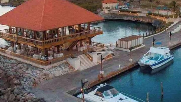 Una marina con un barco amarrado, un edificio de techo rojo y un gran hotel al fondo.