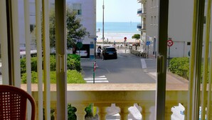 Vue depuis un balcon donnant sur une rue, avec une plage en arrière-plan. On aperçoit des bâtiments, un panneau de signalisation et un panneau indiquant l’interdiction de se garer.