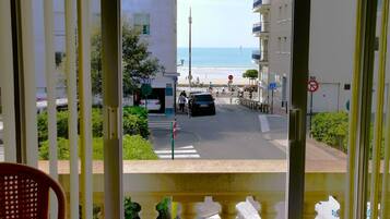 Vue depuis un balcon donnant sur une rue, avec une plage en arrière-plan. On aperçoit des bâtiments, un panneau de signalisation et un panneau indiquant l’interdiction de se garer.