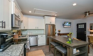 A modern kitchen with white cabinets, stainless steel appliances, granite countertops, and a dining area with a wooden table and bench.