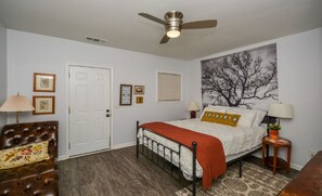A bedroom with a bed, a ceiling fan, a door, and framed pictures on the wall.