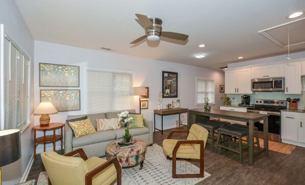 A modern living room with a sofa, chairs, a coffee table, and a dining area with a kitchen in the background.