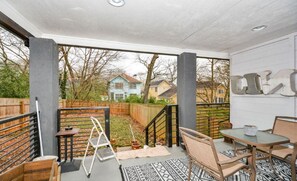 A covered patio with a table and chairs, a ladder, and a view of houses in the background.