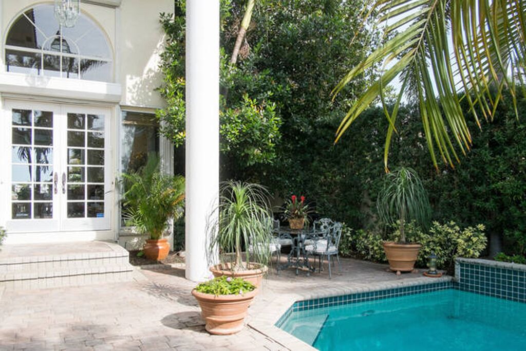 A pool area with a tiled edge, surrounded by potted plants and a patio with outdoor furniture.