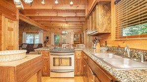 Ein Holzblockhaus-Innenraum mit einer Küche, die sich durch Granit-Arbeitsplatten, Edelstahlgeräte und einen Essbereich mit Tisch und Stühlen auszeichnet.